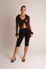 Woman wearing a black lace top with feather details and black pants on a beige background